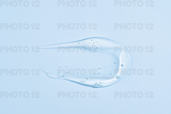 A translucent blue gel-like substance with a smooth, creamy texture, smeared in an elegant, fluid shape against a solid pastel blue background, representing skincare or cosmetic products