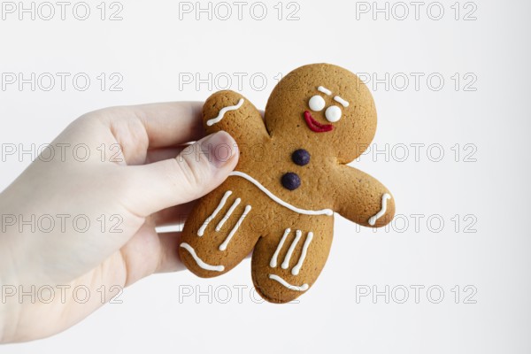 Close-up of a hand holding a cheerful gingerbread man cookie decorated with white icing The background is plain white, highlighting the festive treat's details