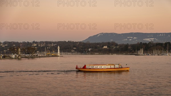 A vibrant yellow boat glides across the serene waters of Lake Geneva during a stunning sunset, with a distant view of a lighthouse and boats anchored on the shore