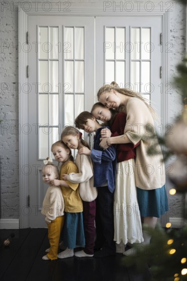 A loving family of six embraces warmly in front of a white-paneled doorway Their cozy clothing and the soft lighting evoke feelings of warmth and holiday cheer