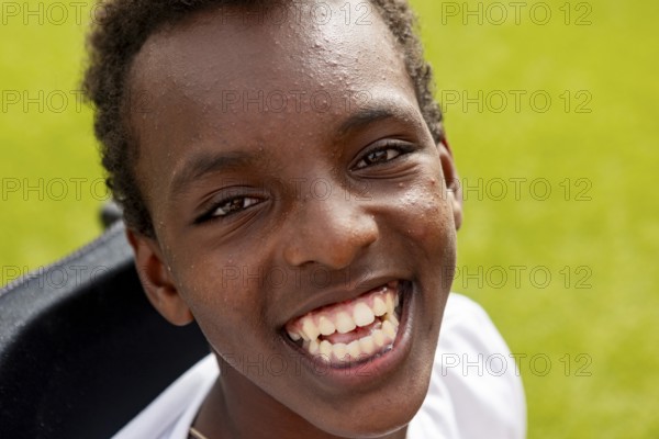 Joyful close-up of a smiling boy with cerebral palsy at surf camp, enjoying a bright sunny day. The boy face radiates with happiness and positivity, set against a vibrant green background
