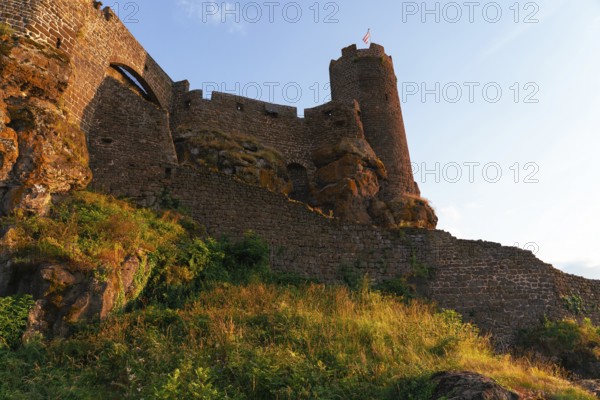 A striking view of the stone walls and towering structures of Chateau Polignac, glowing under the warm hues of sunset The fortress stands amidst grassy terrain, radiating timeless strength