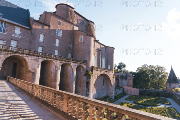 A stunning Berbie Palace exhibits grand architecture, with robust arches and detailed balconies in France The adjacent gardens are meticulously landscaped, bathed in soft sunlight against a clear sky
