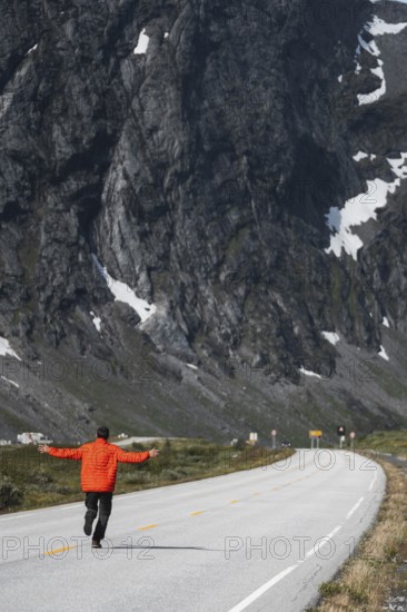 A traveler in a vibrant jacket walks along a winding road, surrounded by Norway's majestic mountains Embrace the spirit of adventure, trekking, and outdoor exploration