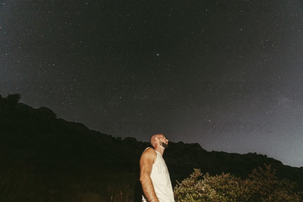 A man gazes upwards, immersed in the wonder of a star-filled night sky The serene landscape and twinkling stars create a sense of exploration and tranquility