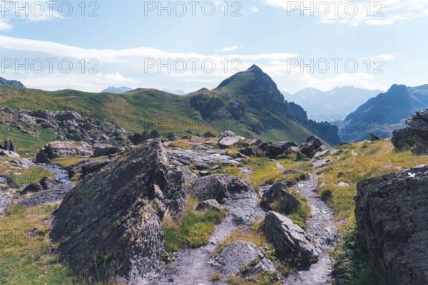 A scenic hiking trail winds through rocky terrain at the Ibones de Anayet in Huesca, Spain, showcasing stunning mountain views and lush, verdant slopes under a clear blue sky