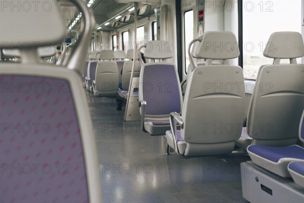 A spacious and well lit interior of a modern train, featuring rows of empty gray seats and purple. The clean and minimalist design offers a comfortable travel ambiance