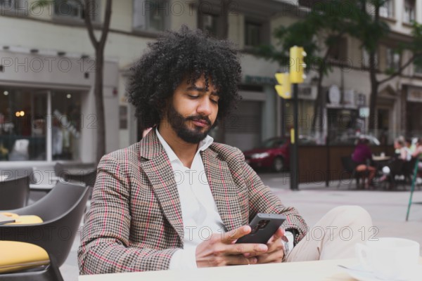 A Mixed-race man with curly hair is engrossed in his smartphone while teleworking on a busy city street, depicting the modern remote work lifestyle