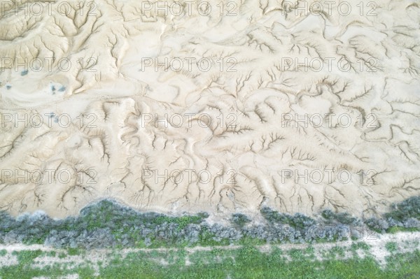 Aerial view of a uniquely textured, arid landscape showcasing patterns of erosion A strip of green vegetation lines the bottom, contrasting the dry terrain above