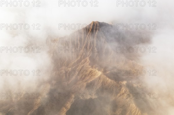 A breathtaking mountain peak emerges through a dense layer of clouds, showcasing its rugged terrain The soft, swirling mist adds an ethereal touch to the scene, enhancing its majestic beauty