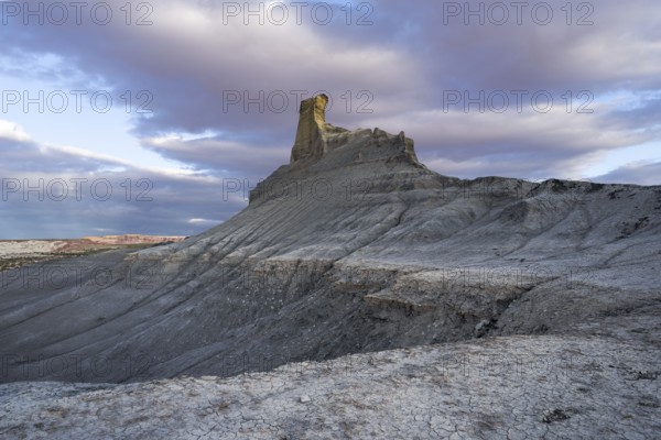 A stunning view of a uniquely shaped rock formation amid textured desert terrain in Utah, captured under a dramatic sky at dusk
