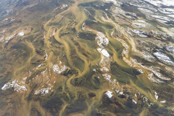 Aerial view of Iceland's rivers showcasing intricate textures and vibrant colors. The landscape highlights winding waterways amidst rugged terrain and snow patches