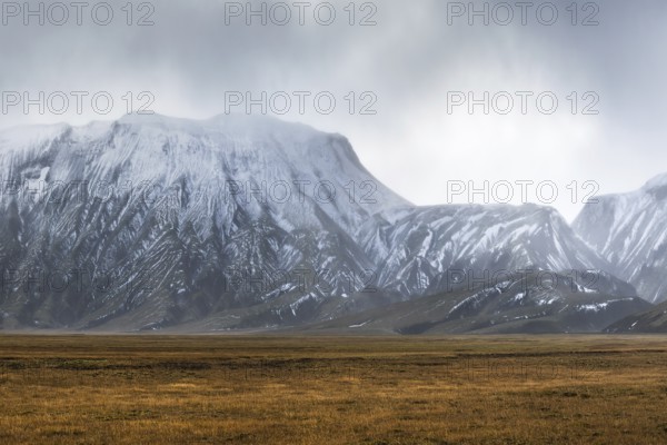 Captivating landscape of the Icelandic Highlands featuring rugged, snow-capped mountains under cloudy skies. Vast open plains stretch in the foreground, conveying solitude and grandeur