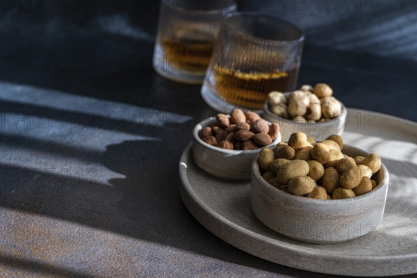 Spiced cognac cocktail accompanied by cinnamon and anise star spice, served with a variety of nuts, almonds, peanuts, and hazelnuts—beautifully arranged on a dark gray textured surface, capturing the interplay of light and shadow