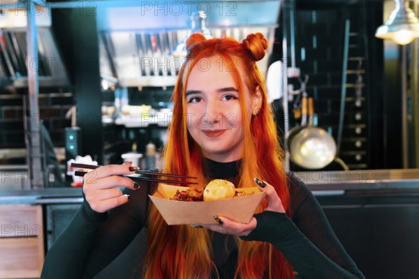 A woman with red hair delights in Asian street food at a lively market She holds chopsticks and a paper tray, surrounded by the bustling ambiance of the market