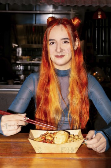 A woman with vibrant red hair sits at an Asian food market, savoring a meal with chopsticks The market's lively atmosphere enhances the cultural experience