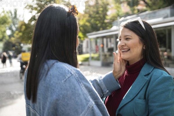 A joyful Latin lesbian couple enjoys a tender moment in a sunlit outdoor setting, expressing love and happiness. They are surrounded by nature and a relaxed atmosphere