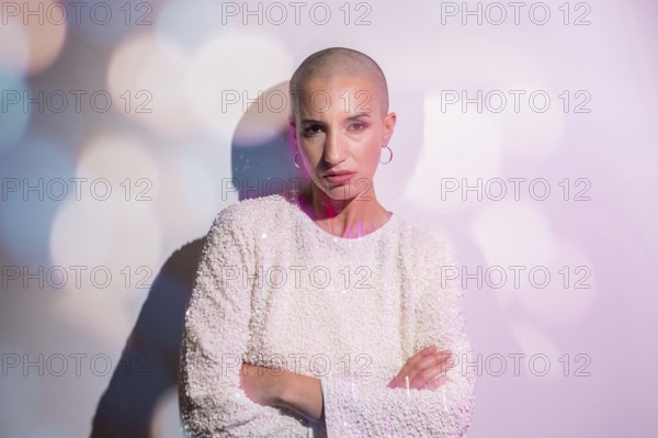 A middle-aged woman with a shaved head stands confidently against a softly lit backdrop, embodying strength and individuality. Her expression is serene and empowering