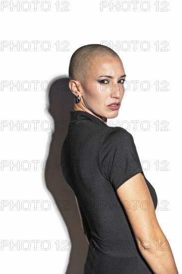 Portrait of a middle-aged woman with a shaved head in a black top, exuding confidence. She is looking over her shoulder, with a calm expression and bold style