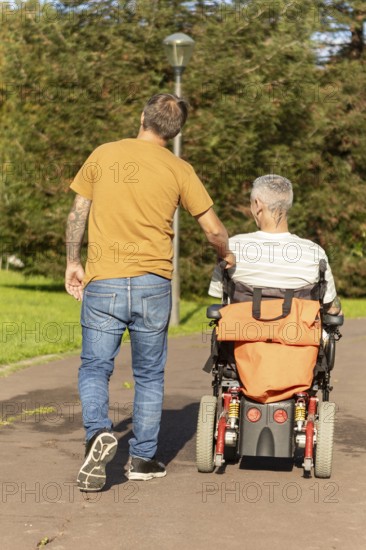 A thoughtful moment capturing a person walking with a friend in a wheelchair with a cerebral palsy along a sunny park path, symbolizing support, friendship, and accessibility in a outdoor setting
