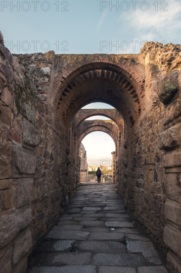 A captivating view through the ancient Roman theatre arches in Merida, Badajoz, Spain. The historic architecture and stone pathway highlight the area's cultural significance
