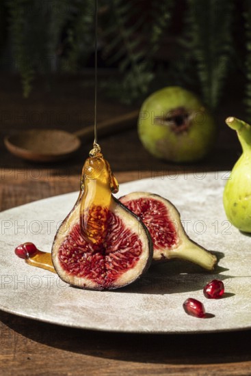 Close up of ripe figs sliced open, drizzled with golden honey. Pomegranate seeds scattered on a ceramic plate. Perfect for food styling or culinary arts themes