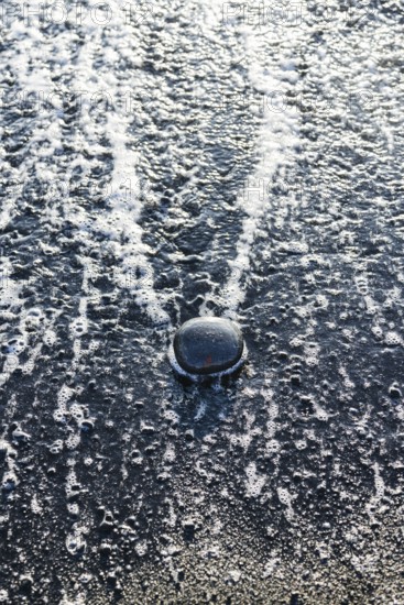 Close-up of water splash on a dark surface with bubbles and foam. The reflection adds a unique texture and dynamic effect