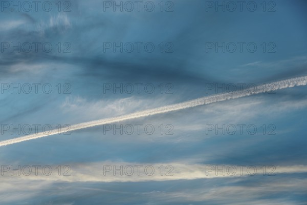 Airplane contrail across a clear blue sky. The white streak contrasts beautifully with the soft clouds in the background