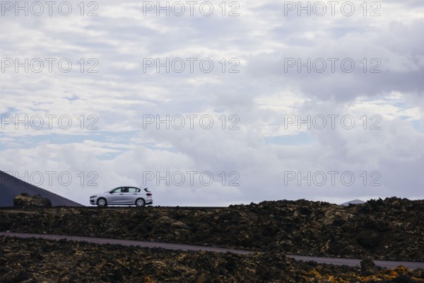 Car on a lonely road surrounded by a volcanic landscape. The rocky formations emphasize the contrast between asphalt and nature