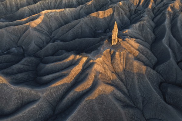 A striking aerial view of the textured terrain of Caineville Mesa near Hanksville, Utah, bathed in the warm golden light of the setting sun, highlighting the unique geological formations
