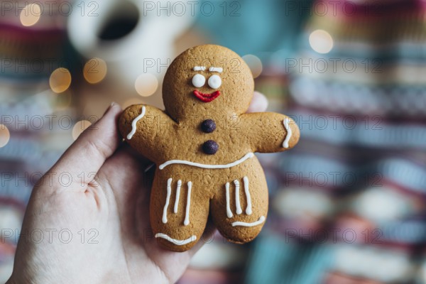 Hand holding a cheerfully decorated gingerbread man cookie, featuring icing details, with a colorful, warm backdrop Perfect for festive and holiday-themed designs