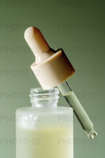 An isolated close-up of a serum dropper bottle with a droplet on a green background, perfect for skincare and beauty themes