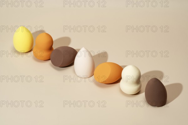 A row of cosmetic sponges in vibrant shades of yellow, orange, and brown displayed on a neutral background Ideal for makeup application, blending, and beauty routines