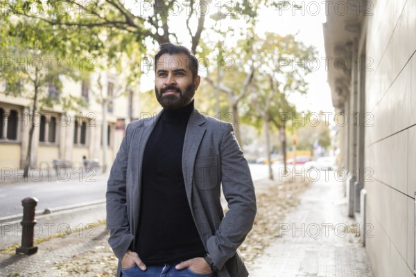 An Indian man, dressed as a businessman in winter attire, strolls along a city street with his hands in pockets, looking away