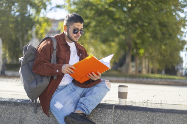 A latino transgender man reads a book in a sunny park He sits on a stone ledge with a backpack and a disposable coffee cup beside him, enjoying a peaceful moment
