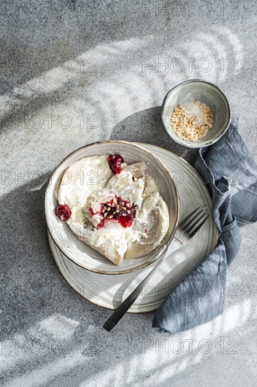 Boiled Ukrainian varenyky filled with cherry, served with a topping of sour cream and chopped nuts in an elegant setting. A delicious and traditional culinary delight