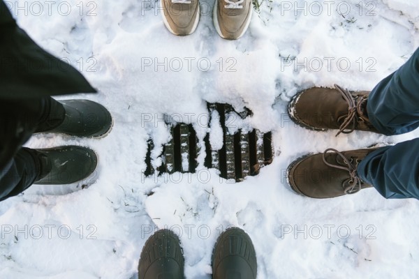Four pairs of shoes and boots encircle a snow-covered drain in Stockholm, capturing a cozy glimpse of winter footwear styles in the Swedish capital