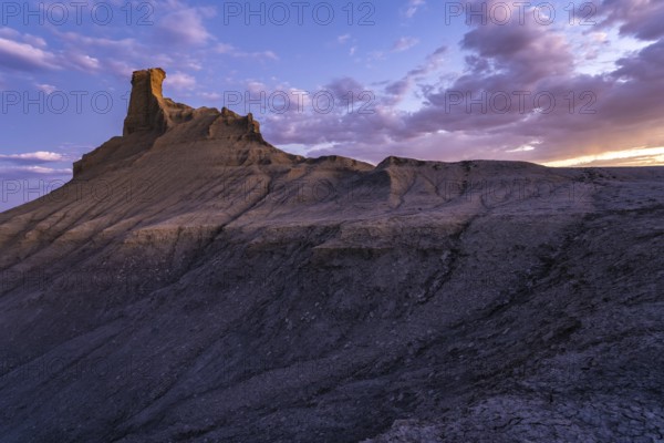 A mesmerizing view of a rock formation in Utah highlighted by the soft glow of a sunset, featuring textured geological layers under a dynamic sky