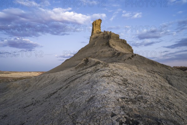 This image captures a striking rock formation in the deserts of Utah, USA, highlighted by a dynamic cloudy sky above and rugged terrain beneath, illustrating the area's natural beauty and geological diversity
