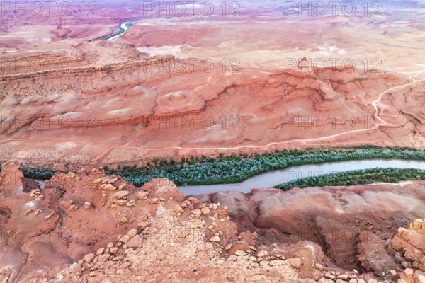Aerial shot captures the serpentine Rio San Juan cutting through the vibrant red desert landscape of Utah, surrounded by rugged terrain and sparse greenery, showcasing dramatic natural contrasts