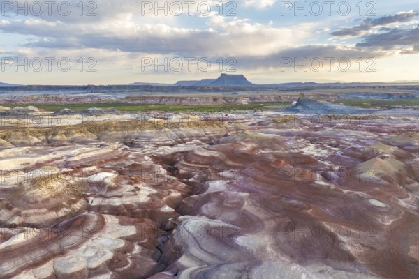 Stunning aerial photograph captures the unique patterns and vibrant colors of bentonite hills in Utah. The landscape showcases intricate natural formations set against a backdrop of vast skies and distant plateaus