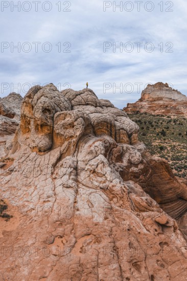 Unrecognizable explorer standing atop a unique swirling rock formation in White Pocket, Arizona, USA. The vast landscape stretches beneath a cloud-covered sky, highlighting the area's rugged beauty