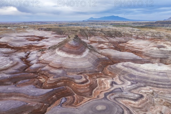 A captivating drone image of an unrecognizable person standing on the unique, multicolored rock layers in the rugged landscapes of Hanksville, Utah, providing a breathtaking natural pattern