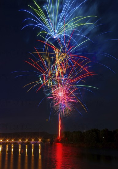 A stunning display of multicolored fireworks illuminates the night sky above the Ebro River, with reflections shimmering in the water below. This vibrant scene captures the beauty and excitement of a festive celebration