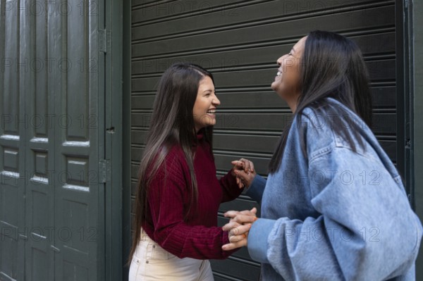 A joyful latin lesbian couple shares a moment of laughter and connection in front of a closed storefront. Their happiness and closeness reflect a deep bond and companionship