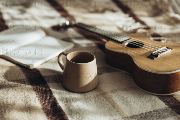 A warm and peaceful morning scene featuring a ukulele, a coffee mug, and an open notebook resting on a soft, patterned blanket, evoking a sense of relaxation and creativity