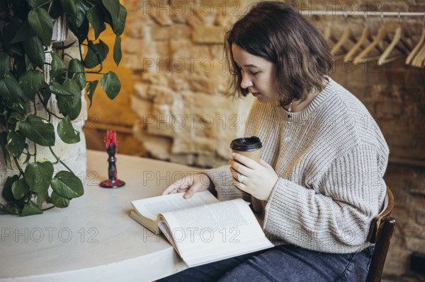 A young woman enjoys reading a book in a cozy bookstore setting She is sipping coffee, surrounded by greenery and warm, inviting decor, creating a tranquil atmosphere