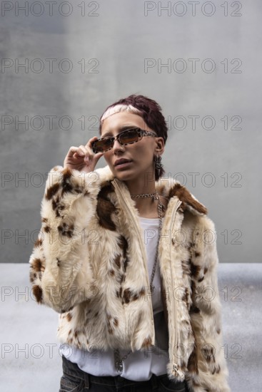 Stylish woman poses in a faux fur jacket and edgy eyewear. Urban setting enhances the chic look, merging fashion with street style. A mix of attitude and elegance