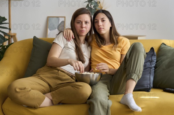 A loving lesbian couple is sitting on a comfortable sofa, enjoying a movie night with popcorn Their relaxed and affectionate demeanor reflects love and togetherness