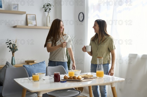A lesbian couple shares a cozy morning breakfast at home They smile warmly at each other, holding coffee mugs, surrounded by a bright and inviting atmosphere